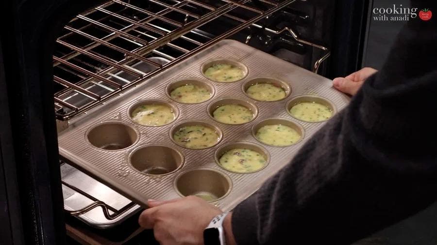 Muffin tray filled with egg mixture in a preheated oven during baking.
