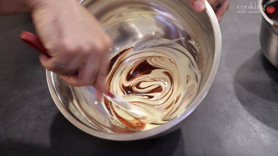 Folding chocolate into egg white mixture with a spatula in a glass bowl to make mousse.