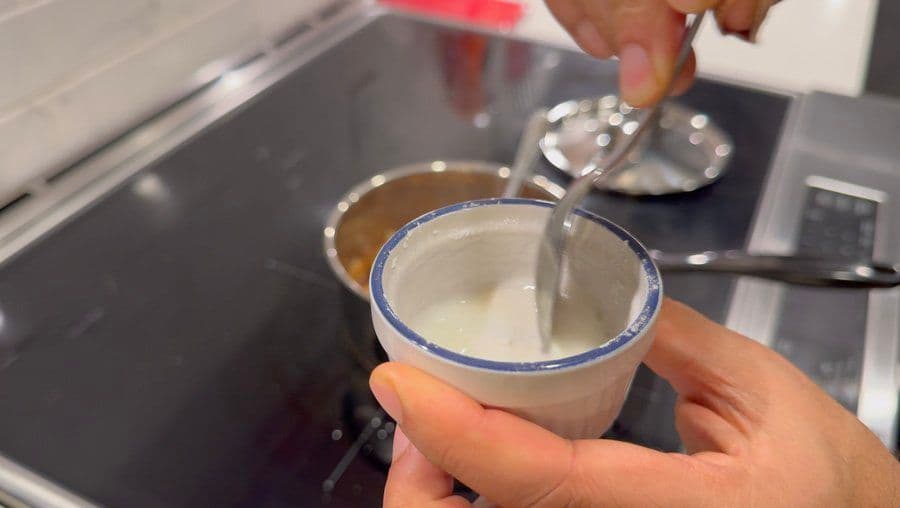 Hand holding a small bowl of cooked apple pie filling with blue rim, showing soft, thickened texture.