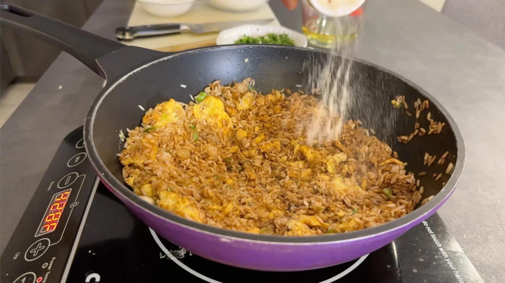 Egg fried rice being tossed in a purple wok with green onions and chilies being added from above.