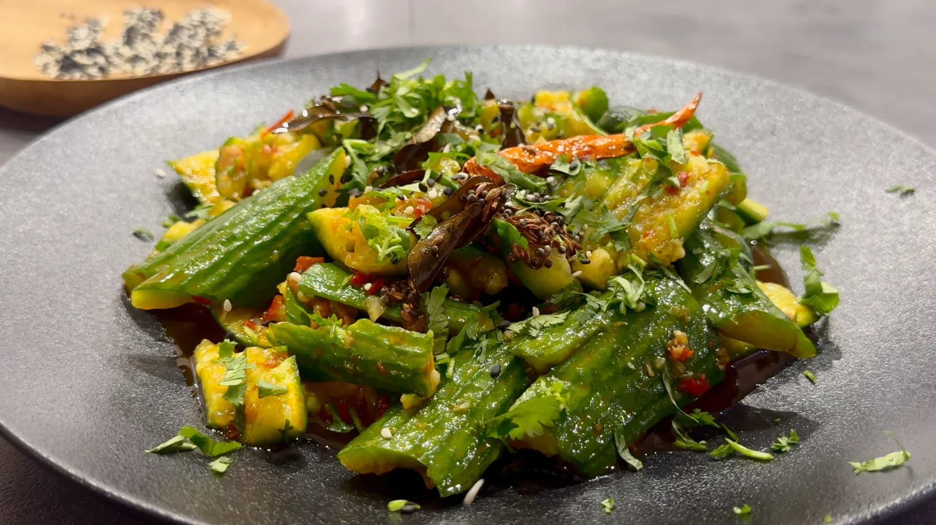 Indian Fusion Smashed Cucumber Salad garnished with cilantro and sesame seeds on a gray plate.