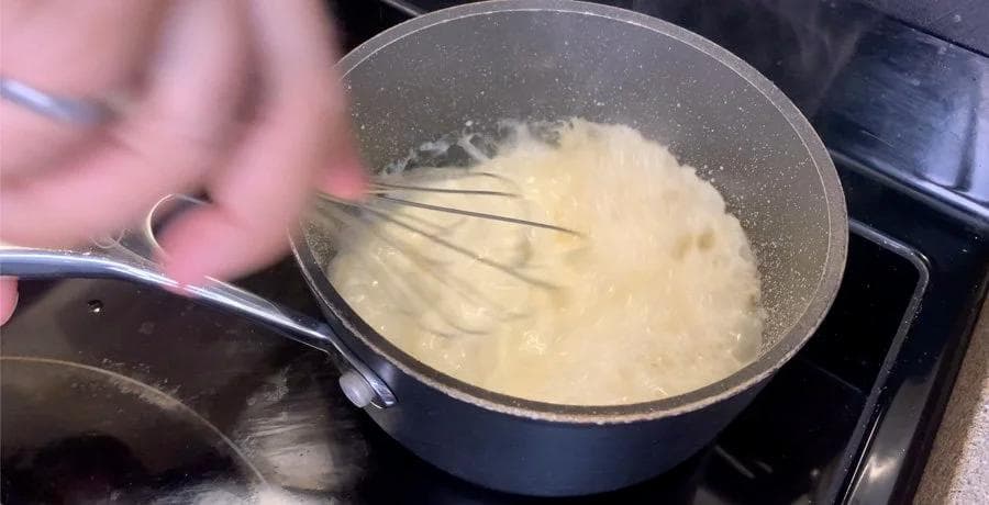 Cream being whisked into caramel sauce in a saucepan on the stovetop
