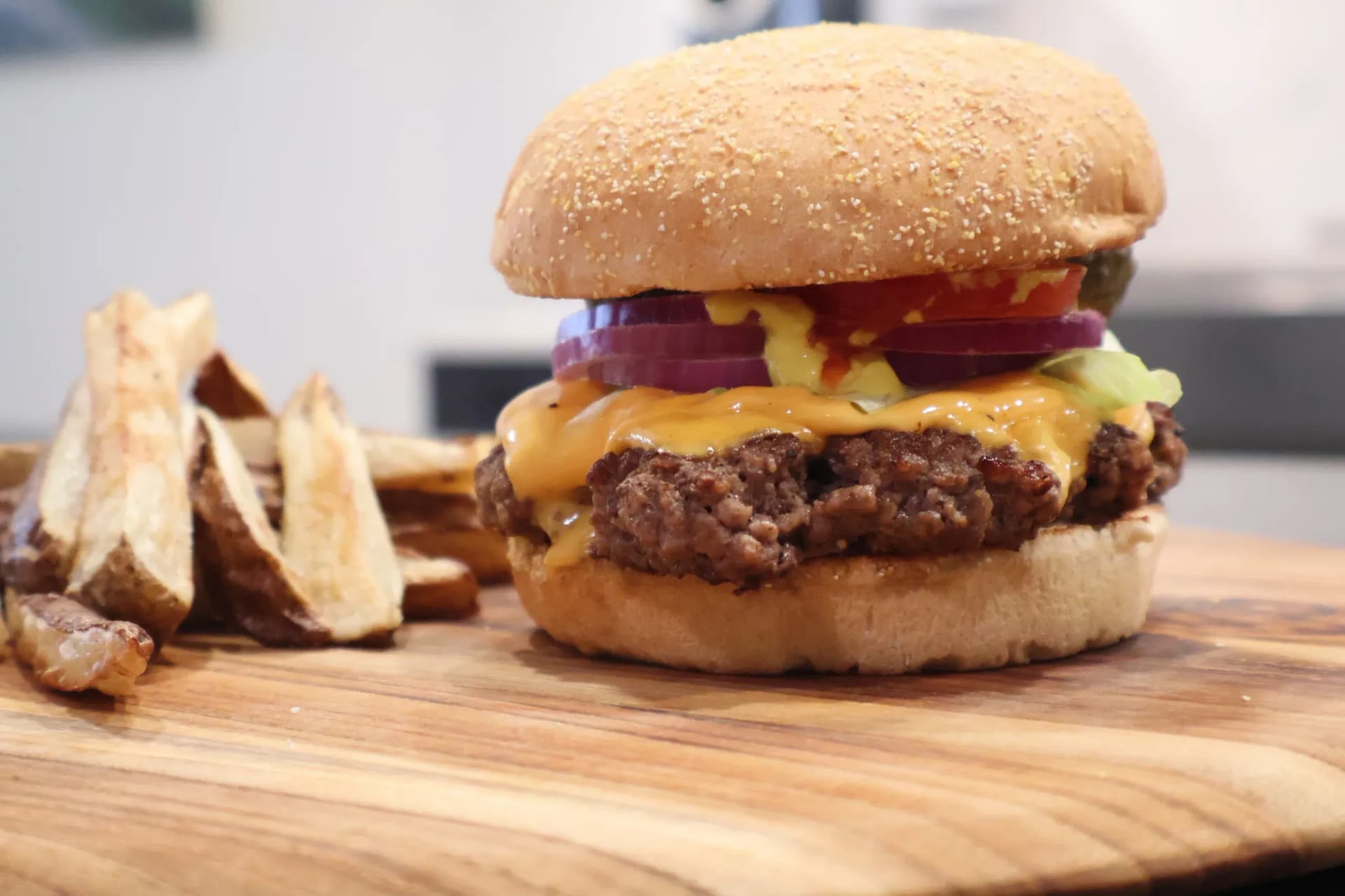 Juicy cheeseburger with melted cheese and red onion on sesame seed bun, served with potato wedges.