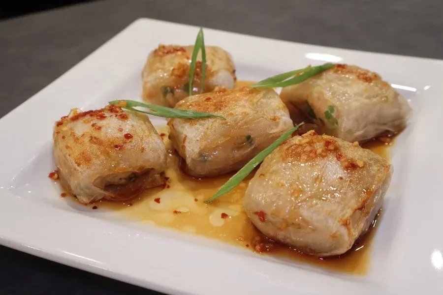 Four golden-brown air fryer rice paper chicken dumplings on a white plate with sauce and green onion garnish.