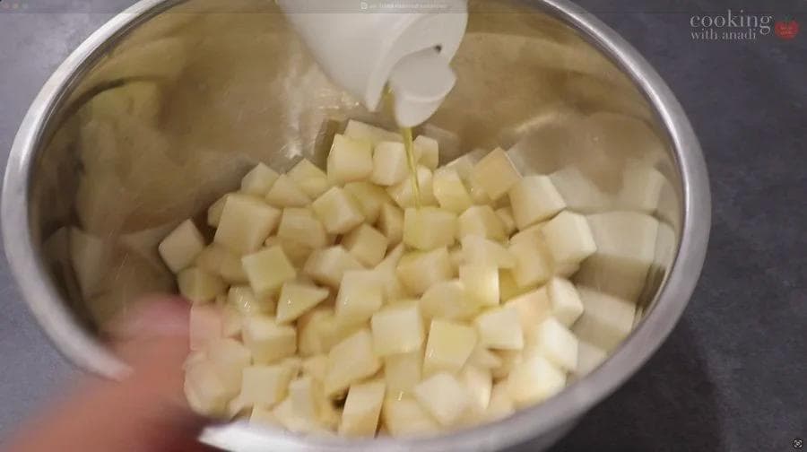 Diced potatoes being transferred into a stainless steel bowl for air fryer cooking