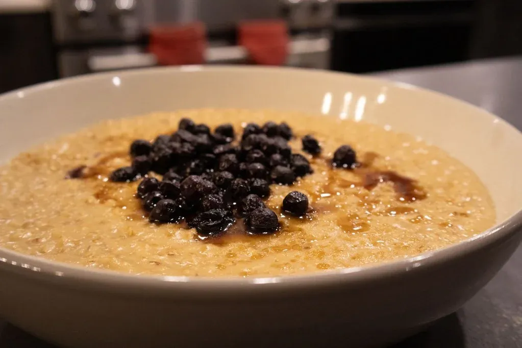 Bowl of creamy steel-cut oatmeal topped with dark raisins and a sprinkle of brown sugar.