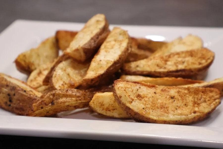 Crispy golden-brown Cajun potato wedges seasoned with spices on a white plate.