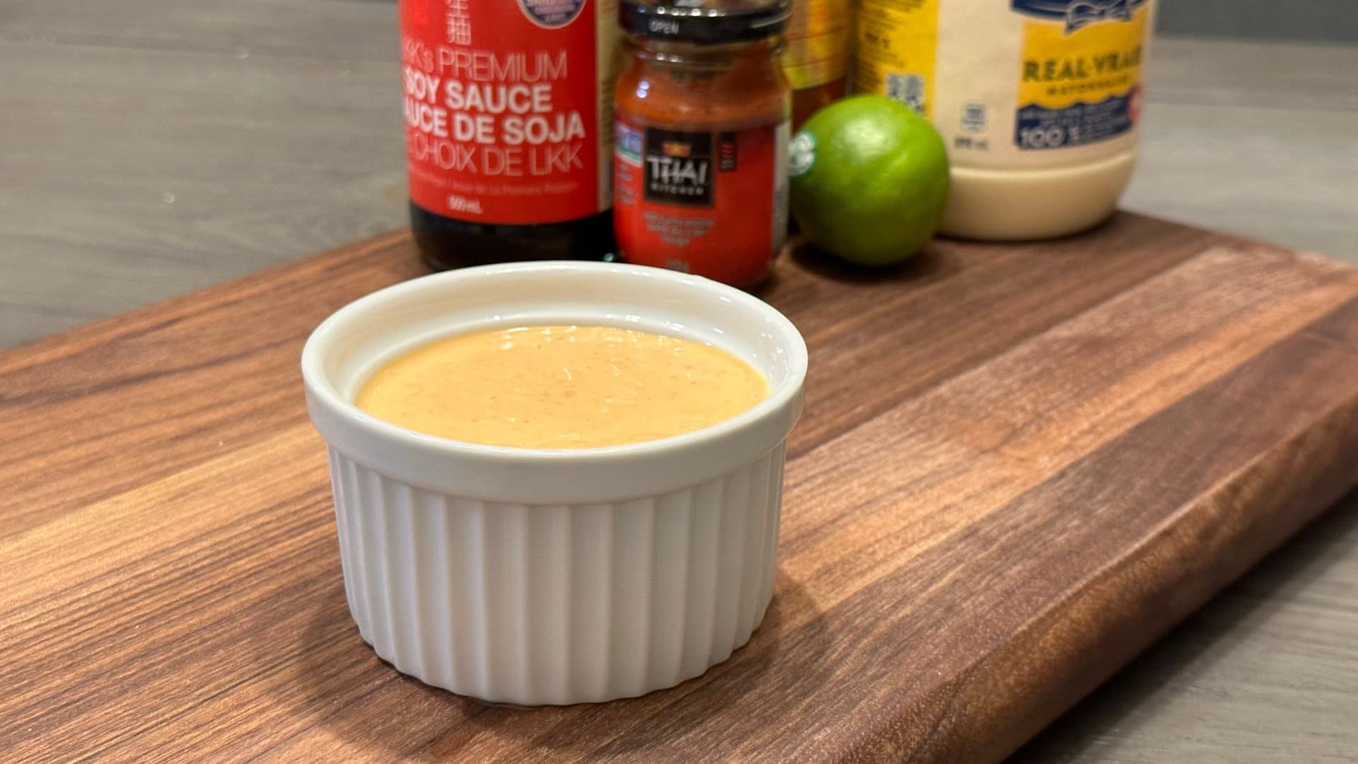 Homemade Thai curry mayonnaise in a white ramekin with soy sauce, Thai chili paste, lime, and peanut sauce in background.