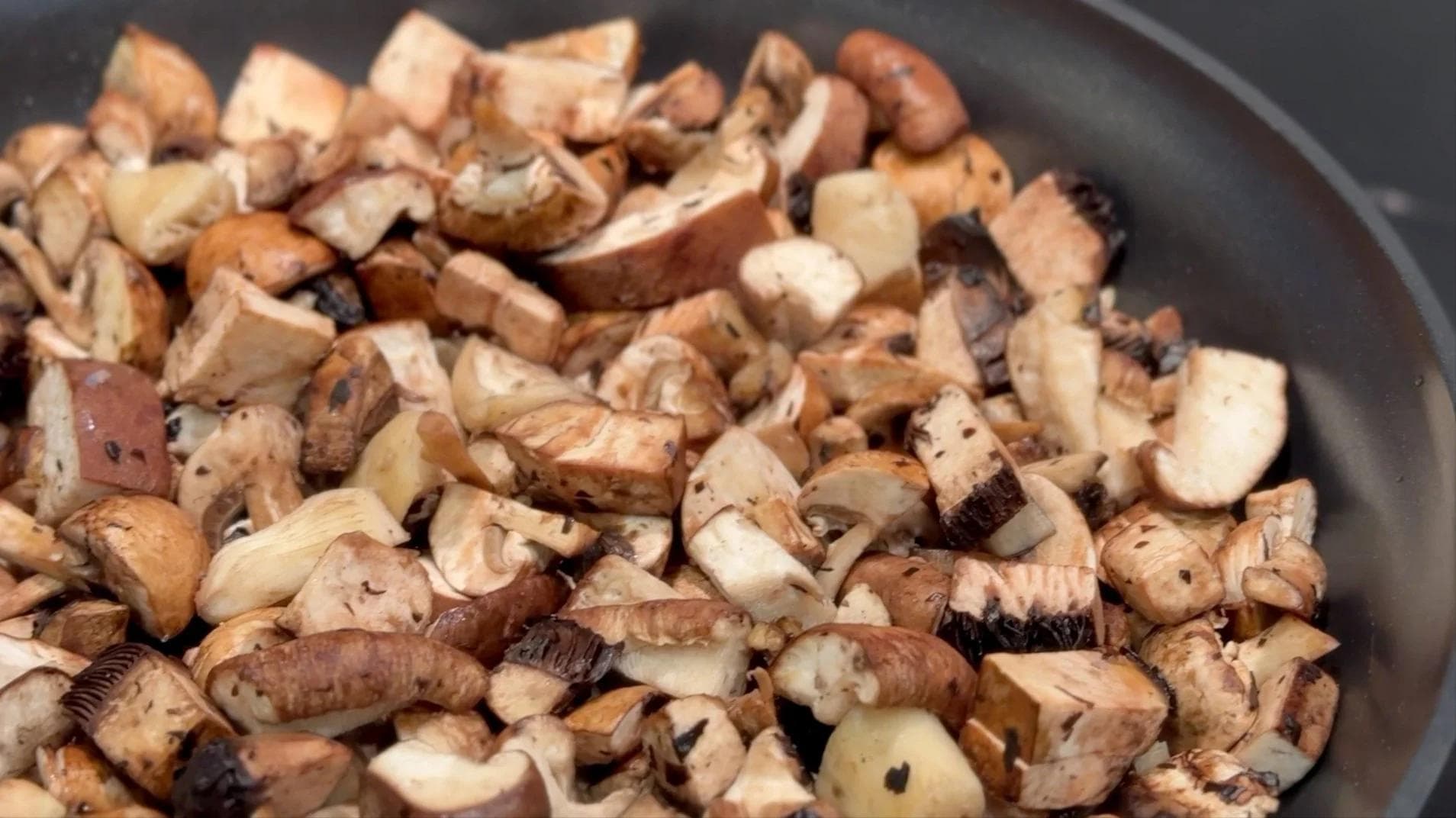 Diced mushrooms cooking in a pan, partially reduced and beginning to release their juices