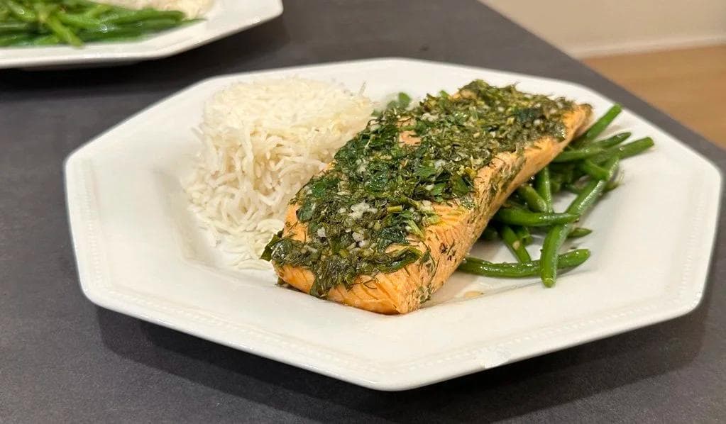 Herb-crusted baked salmon fillet with green beans and rice noodles on a white plate