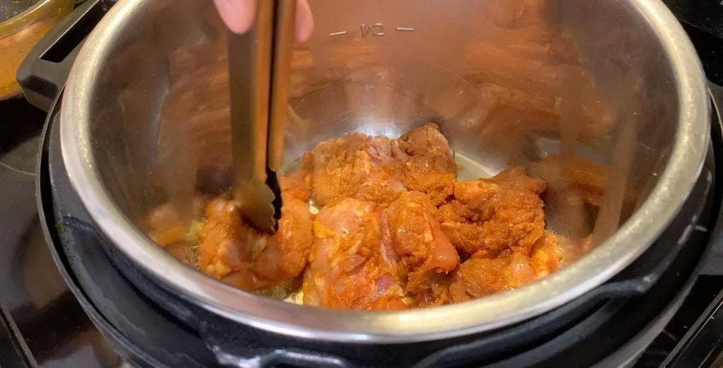 Browned chicken pieces being stirred in an Instant Pot during the sauté step of Arroz Con Pollo preparation.