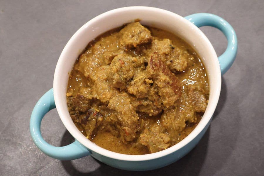 Stovetop Balinese beef rendang in a turquoise and white serving bowl, showing tender meat pieces in rich brown curry sauce.