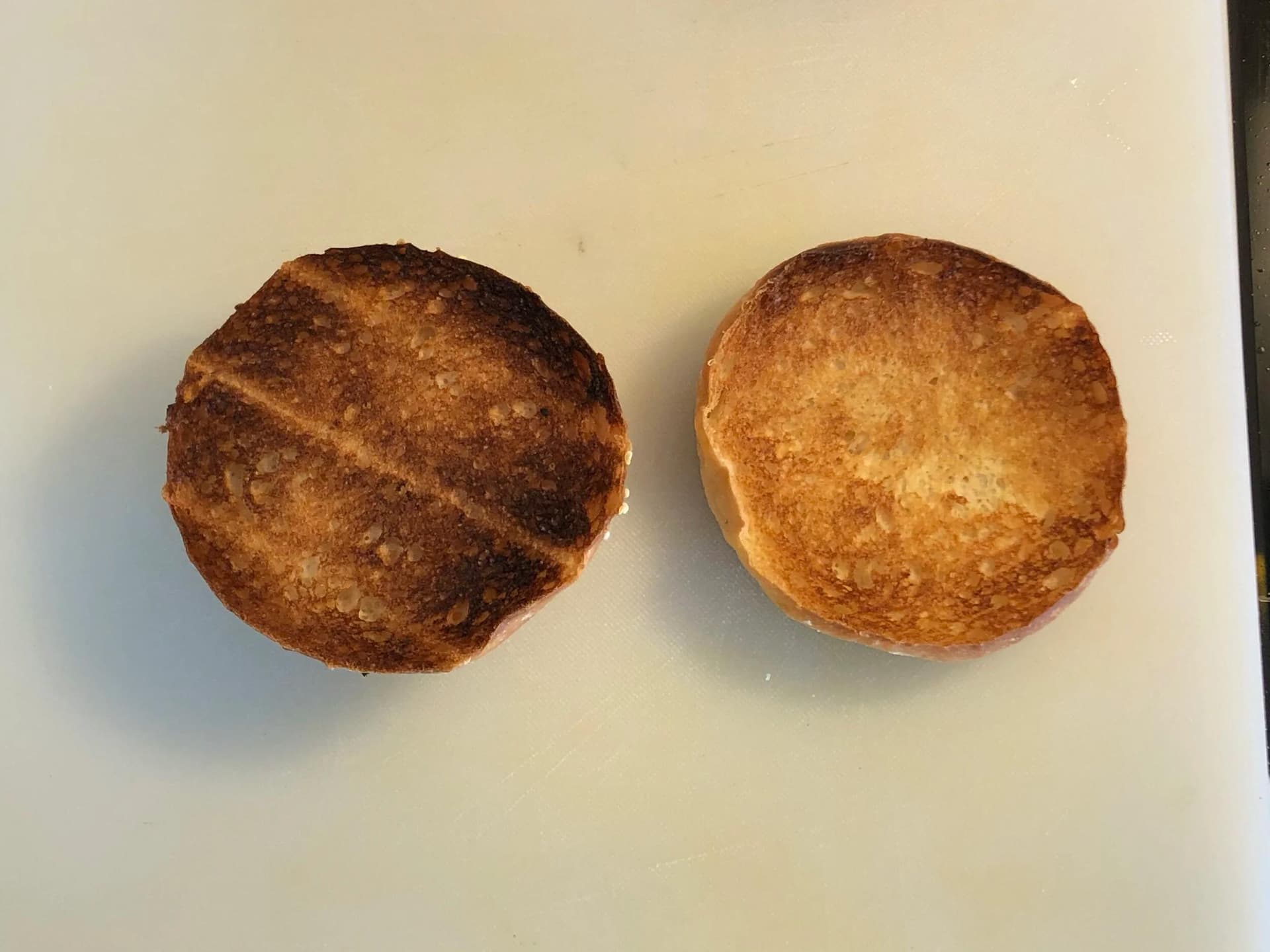 Two toasted burger buns on a white plate, golden brown with sesame seeds.