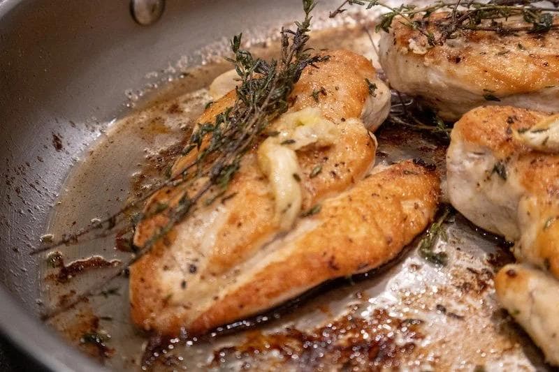 Golden pan-seared chicken breasts with fresh thyme sprigs and garlic in a skillet with browned butter.