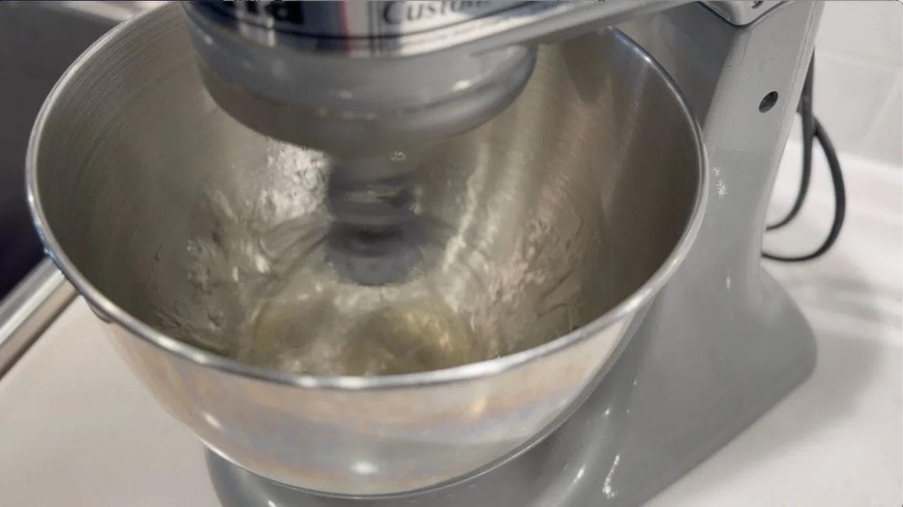 Stand mixer with whipped egg whites at soft peak stage in stainless steel bowl.