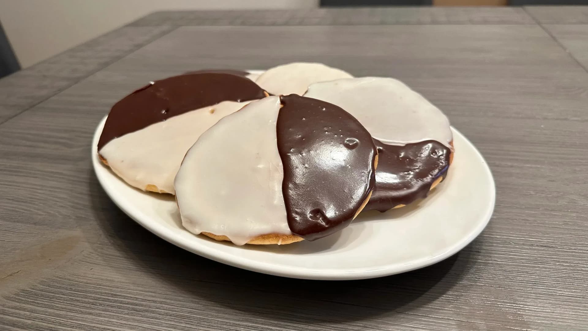 Three New York black and white cookies on a white plate, showing dark chocolate and white icing glazed halves.