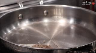 Cumin seeds toasting in ghee in a stainless steel pan on medium heat for dal makhani tadka.