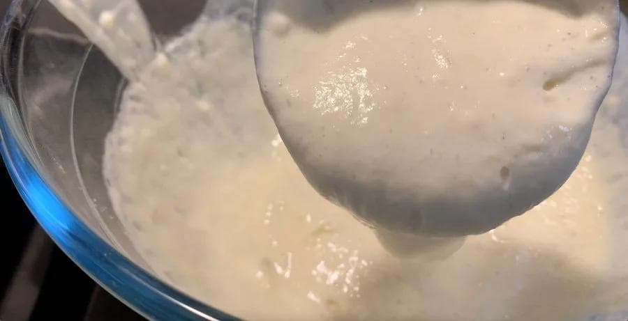 Thick pancake batter being lifted with a whisk, showing its runny consistency in a mixing bowl.