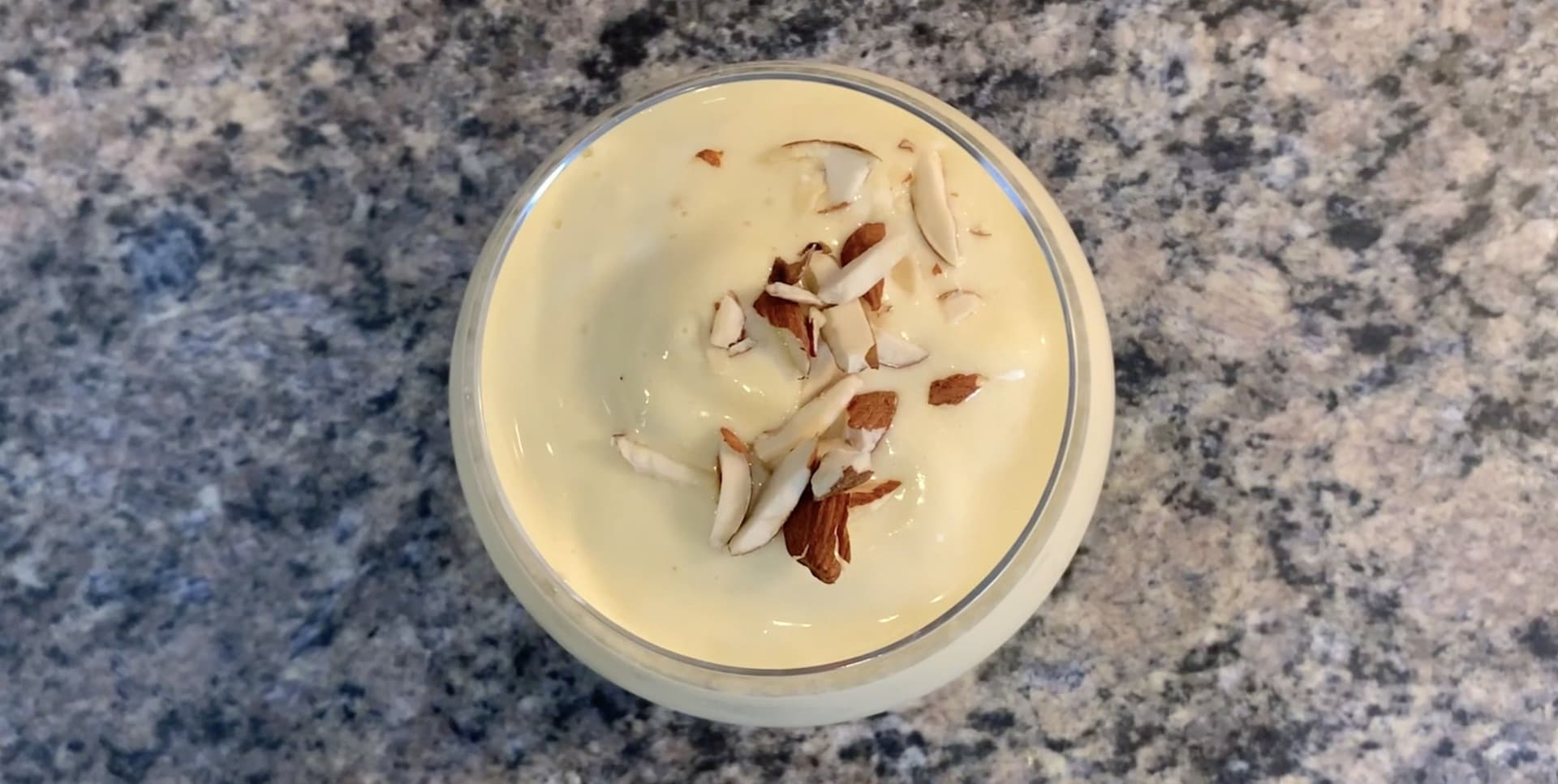 Mango lassi in a glass bowl topped with sliced almonds on a granite countertop.