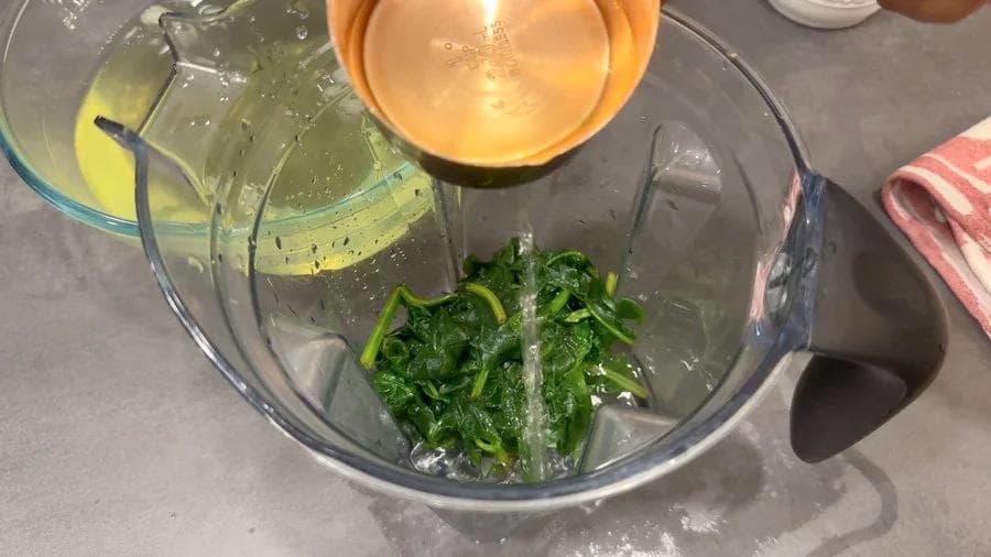 Blended spinach puree in a glass bowl with oil and water being poured in during Palak Paratha preparation.