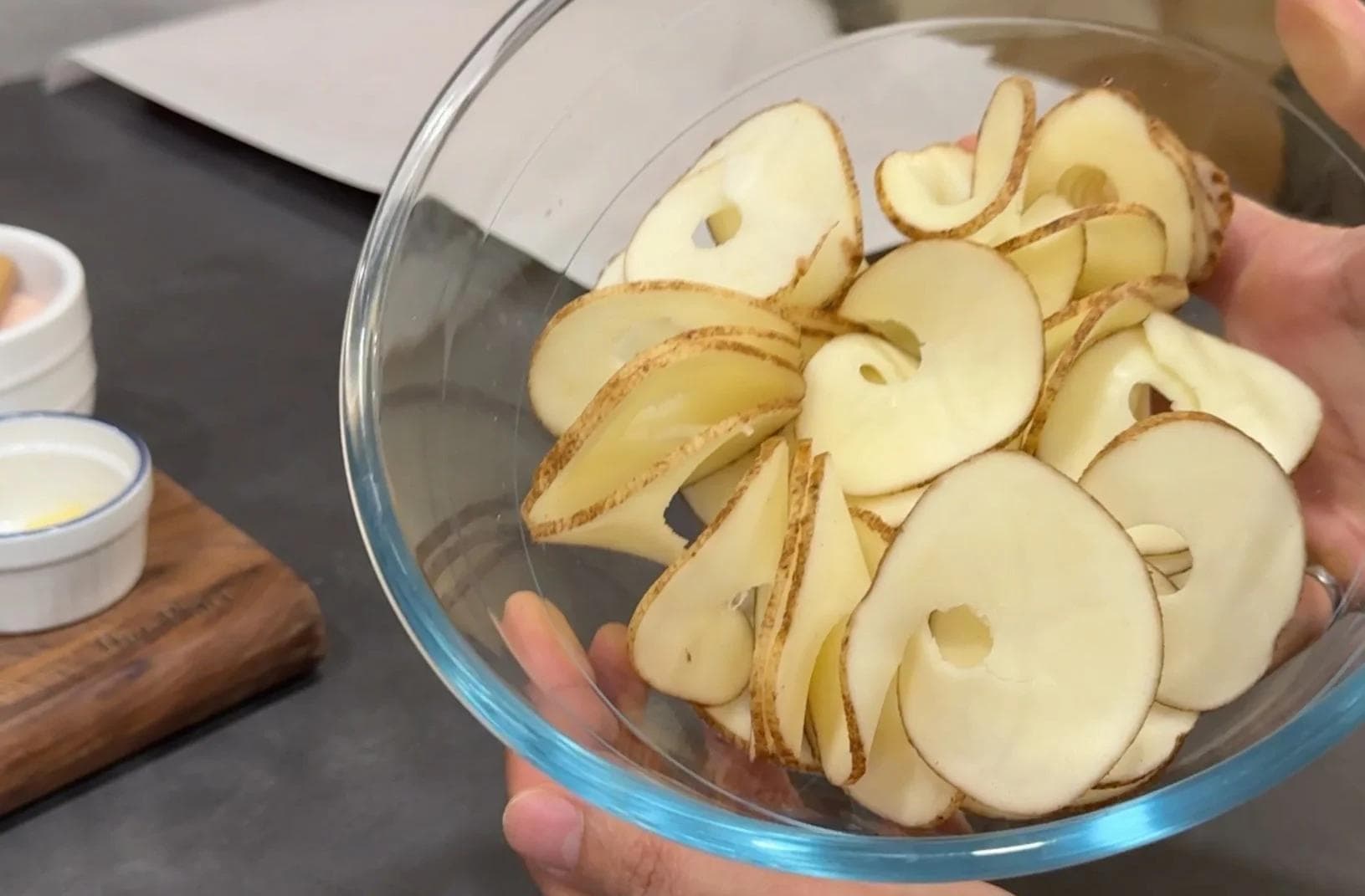 Thinly sliced potatoes in a glass bowl, showing spiralized and layered potato slices.
