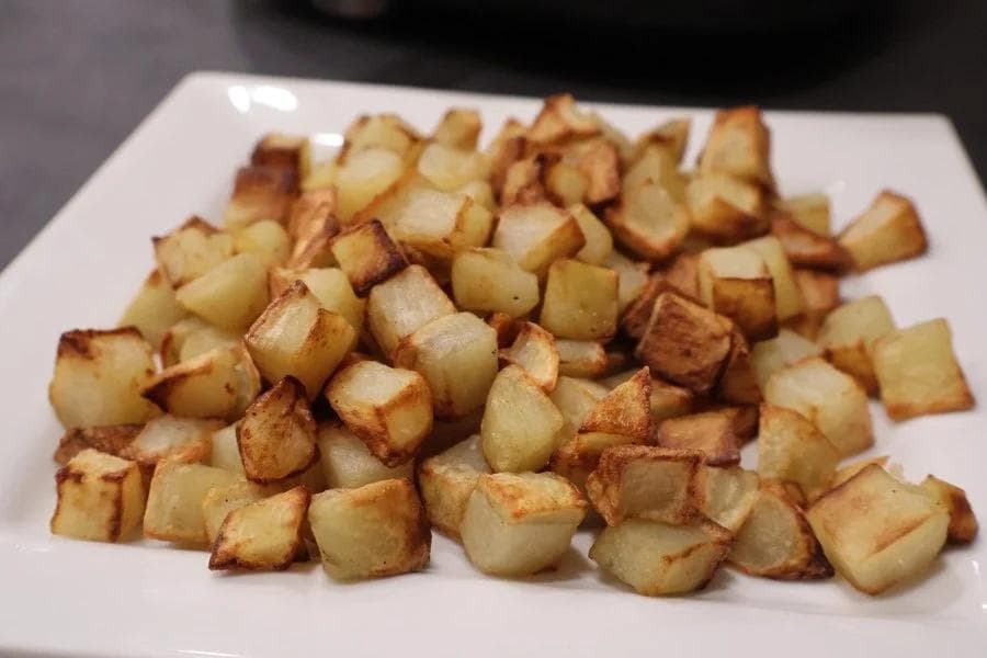 Crispy golden roasted potato cubes on a white plate, cooked until browned and tender.