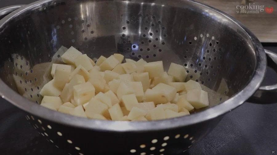 Diced potatoes in a stainless steel colander, ready to be seasoned for air frying.
