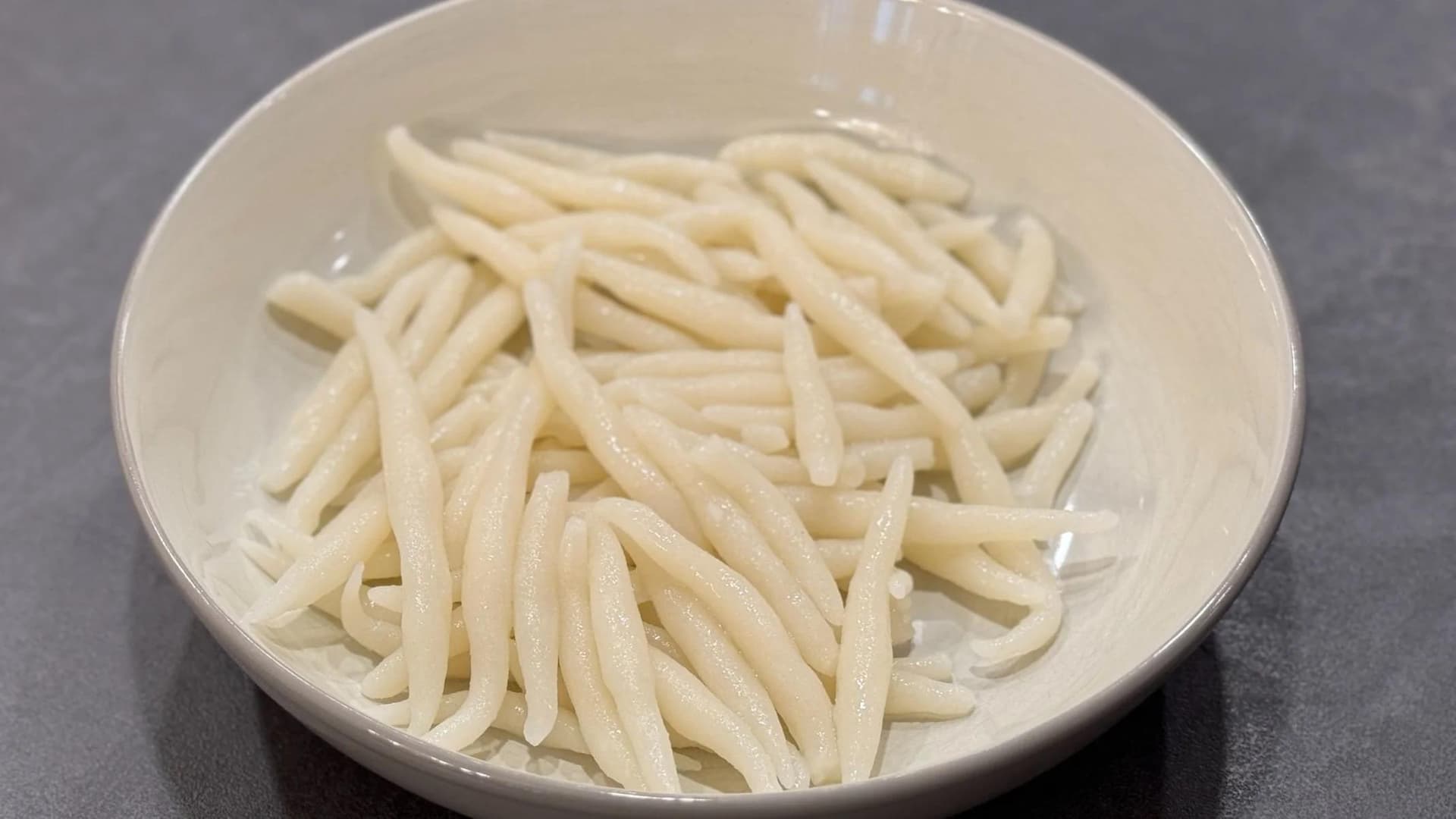 Cooked rice pin noodles piled in a white bowl, showing their thin, delicate strand texture.