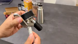 Hand holding a whipped cream dispenser with black tip and metal head over a kitchen counter.