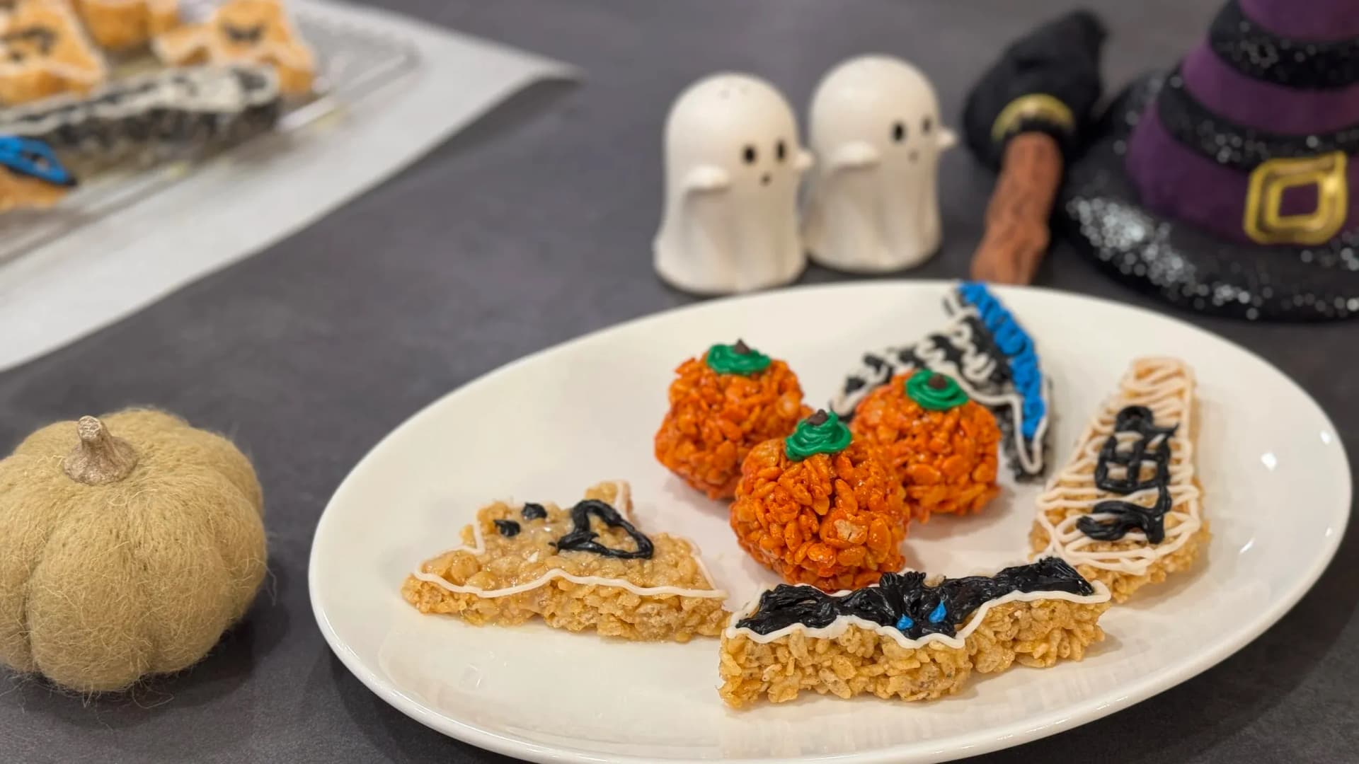 Halloween-themed Rice Krispies treats shaped as pumpkins and bats arranged on a white plate with festive decorations.