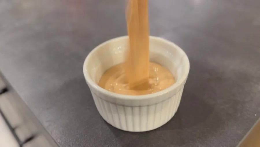 Homemade burger sauce being drizzled from a wooden spoon into a white ramekin.