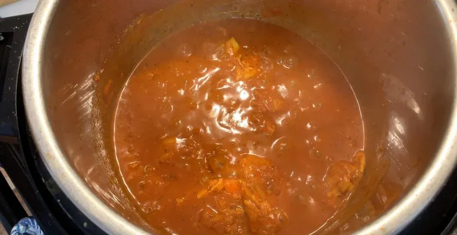 Simmering chicken tikka masala sauce in an Instant Pot, showing a rich orange-brown curry base.
