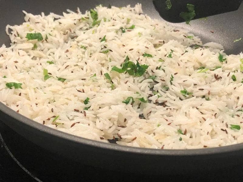 Cooked jeera rice in a dark pan garnished with fresh cilantro and toasted cumin seeds