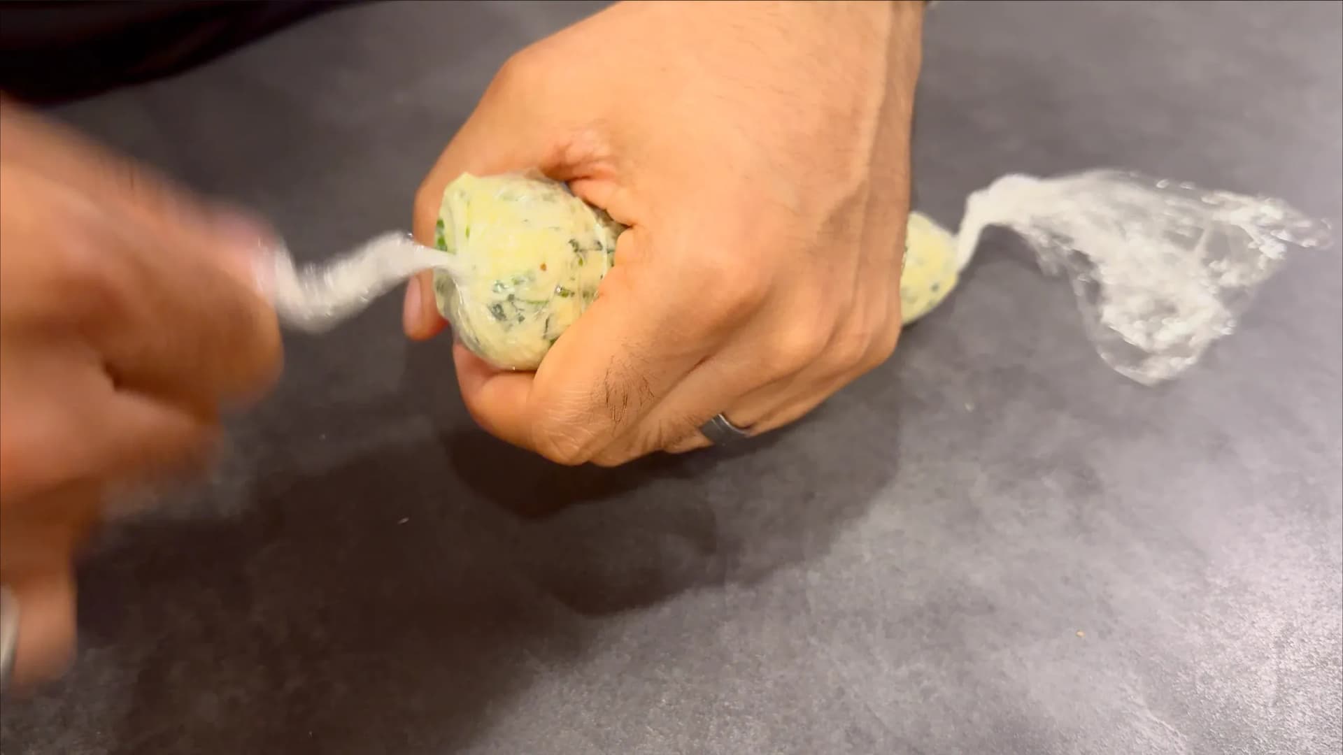 Hand holding a log of garlic herb butter wrapped in plastic wrap, twisted at the ends.