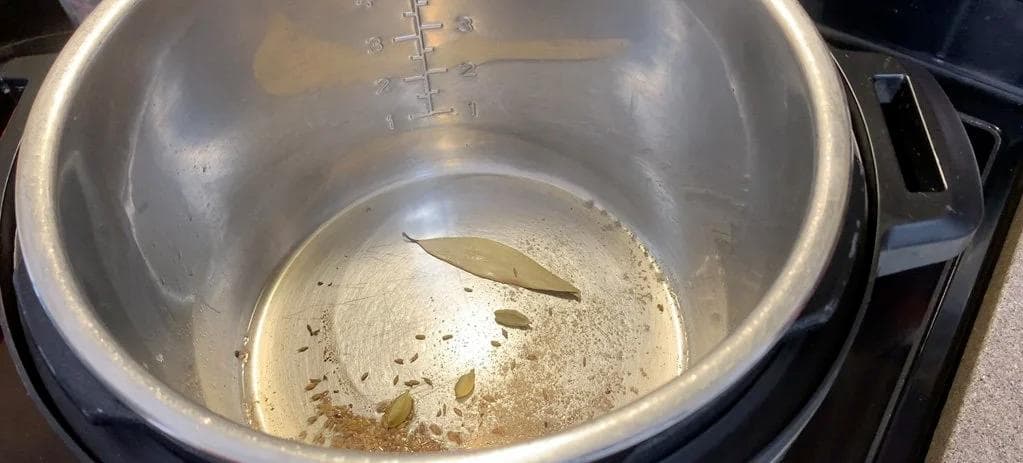 Instant Pot with melted ghee, cumin seeds, cardamom pods, bay leaf, and partially cooked onions during sautéing.