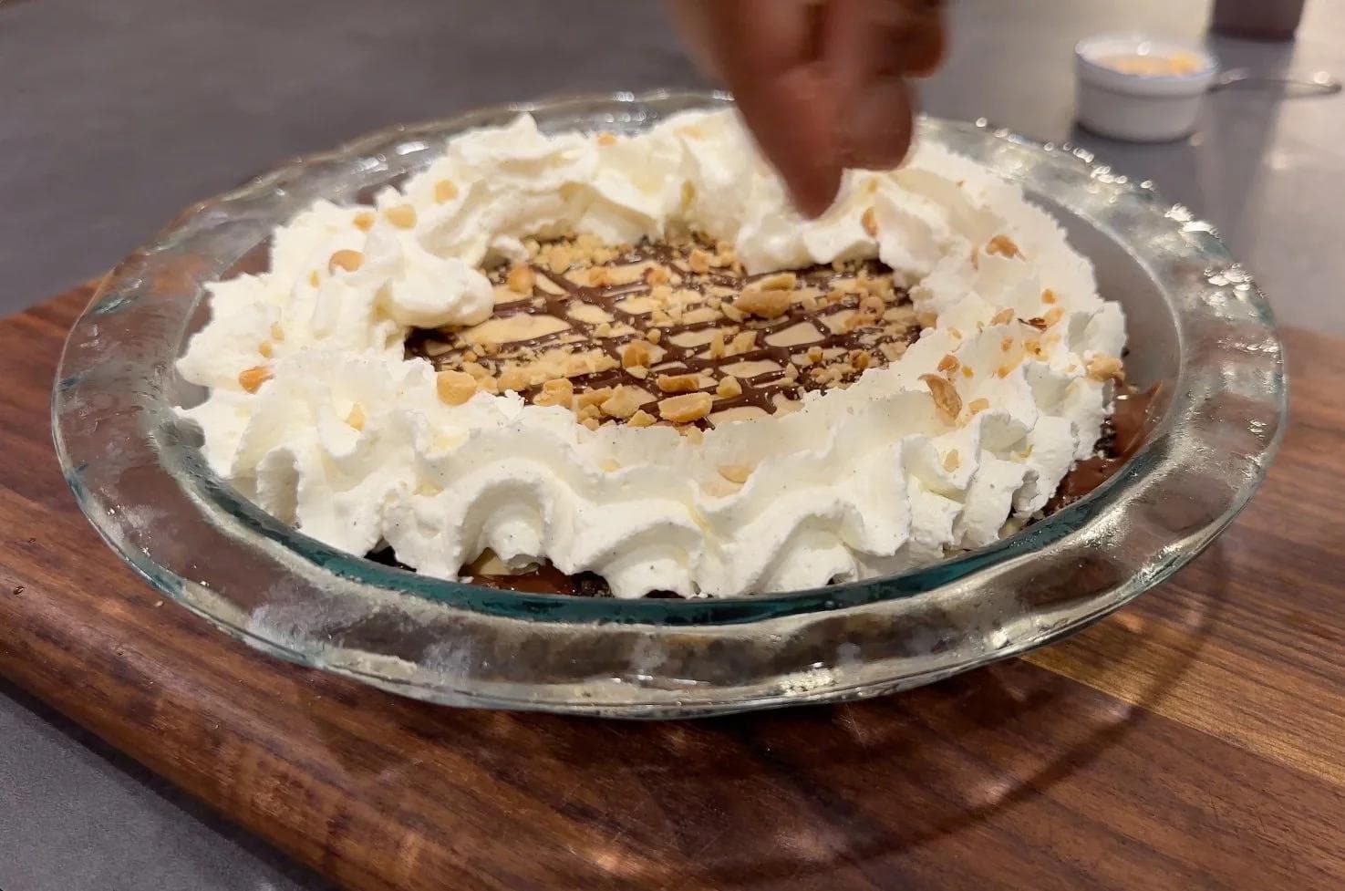 Creamy no-bake peanut butter pie topped with whipped cream, chopped peanuts, and chocolate drizzle in a glass pie dish.