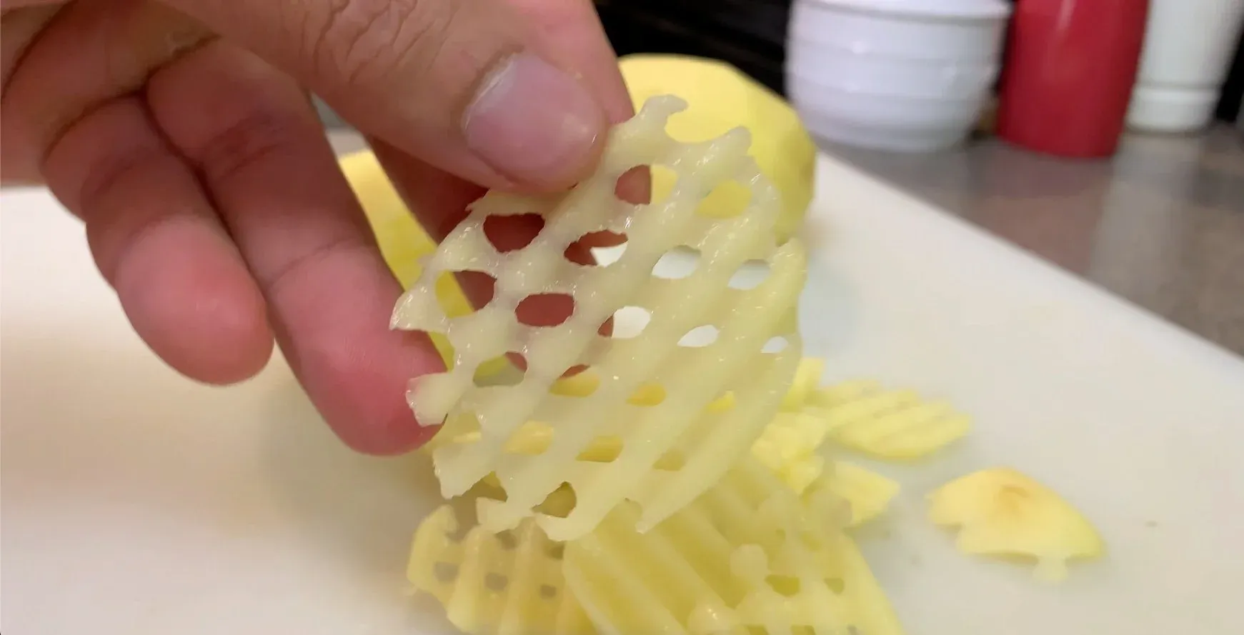 Hand holding a crinkle-cut waffle fry showing the crosshatch pattern of cuts in the raw potato.