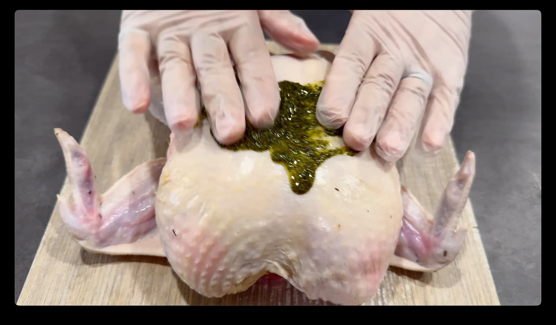Hands rubbing herb paste under the wings and into slits of a raw whole chicken on a cutting board.
