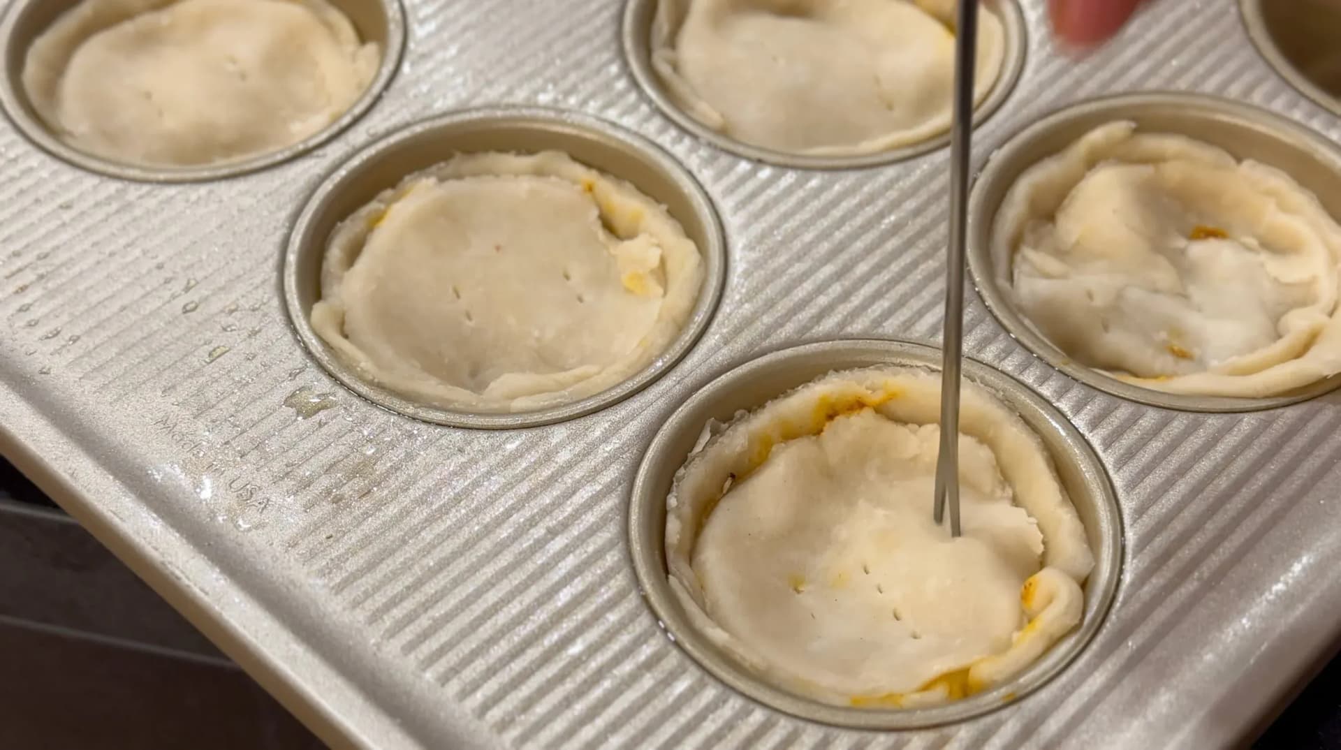 Belizean meat pies in a muffin tin before baking, showing egg wash applied to pastry tops.