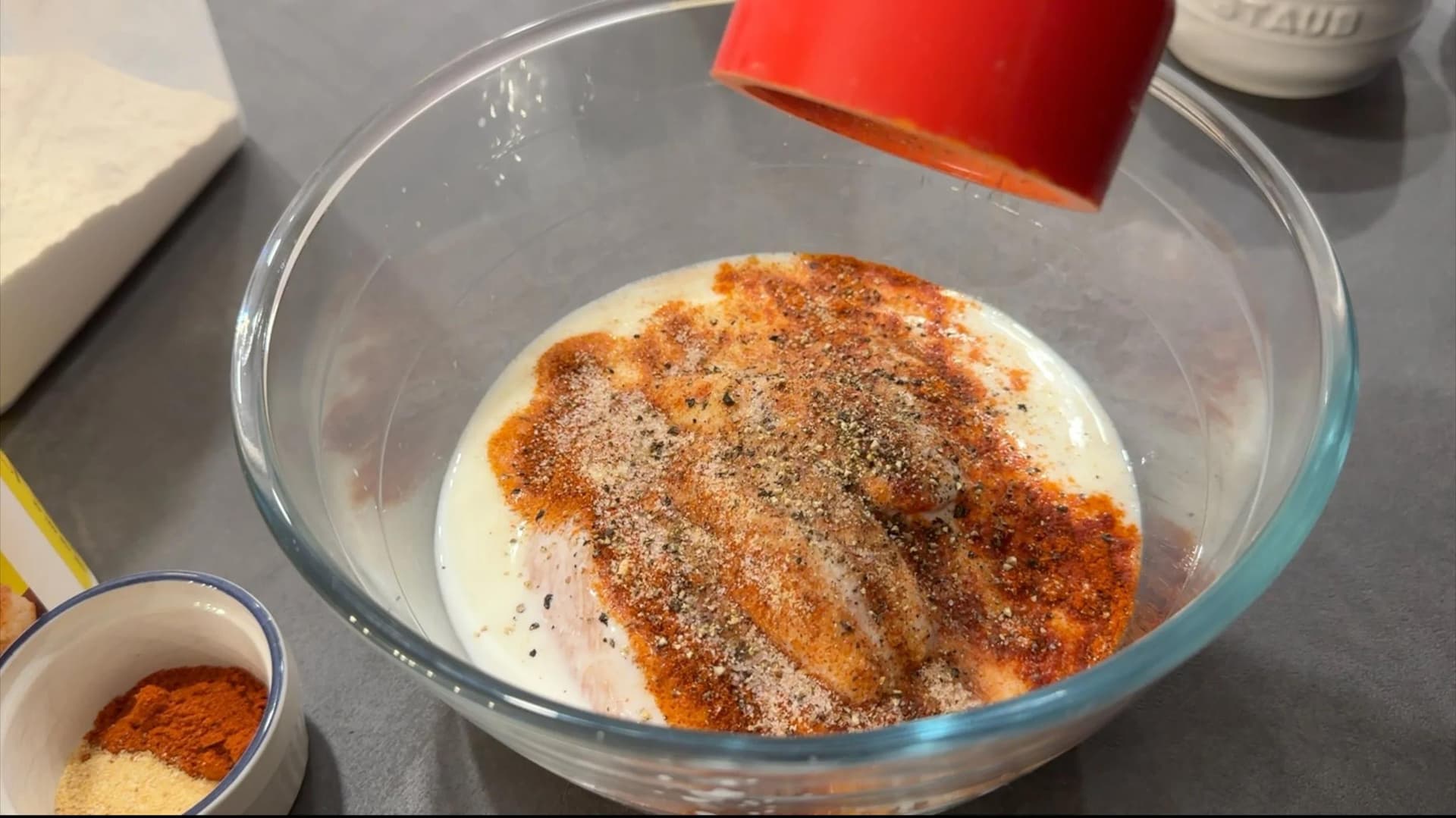 Spice mixture and buttermilk added to chicken tenders in a glass bowl for marinating.