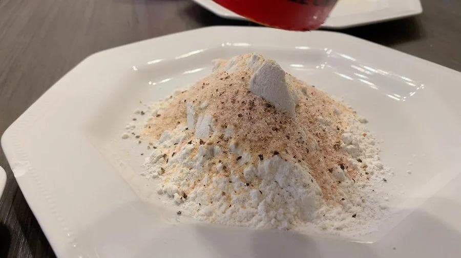 Seasoned flour mixture in a white bowl for breading mozzarella balls, with garlic powder and black pepper visible.