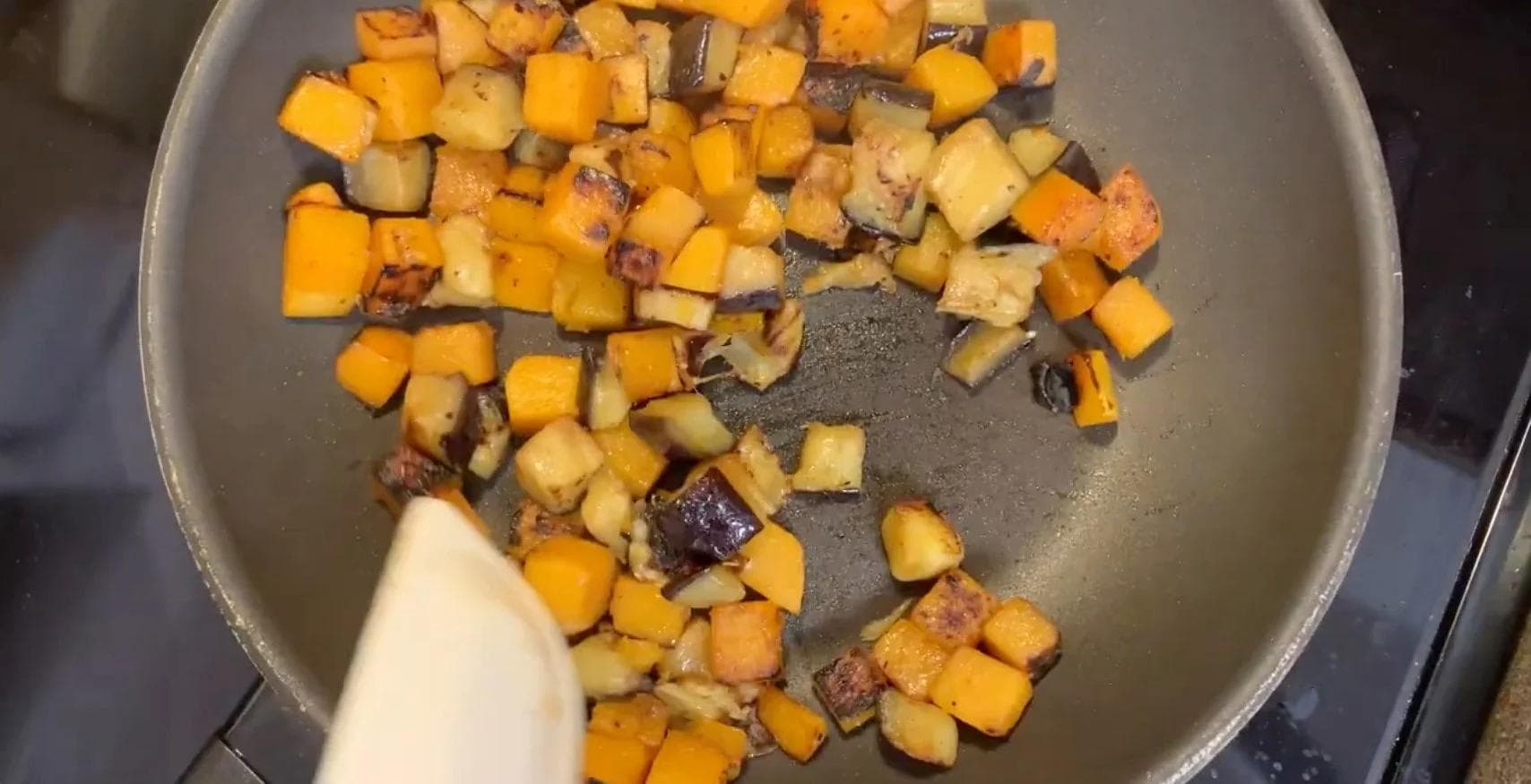 Diced squash and eggplant with light browning in a gray pan on stovetop.