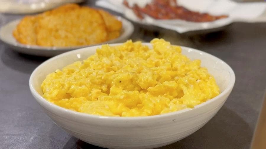 Fluffy scrambled eggs in a white bowl, slightly runny and ready for breakfast burritos.
