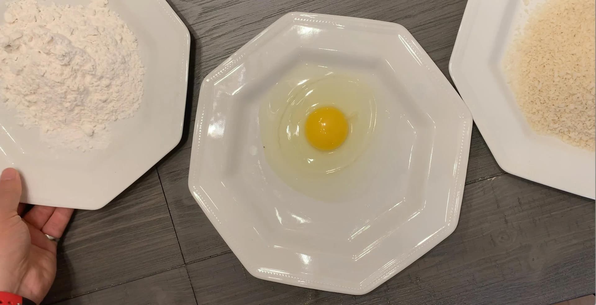 Three white plates with flour, whisked egg, and breadcrumbs for breading McAloo Tikki patties.