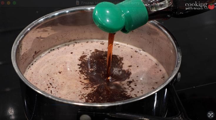 Pouring hot chocolate mixture into a saucepan with a green handle, showing combined chocolate and cream ingredients.