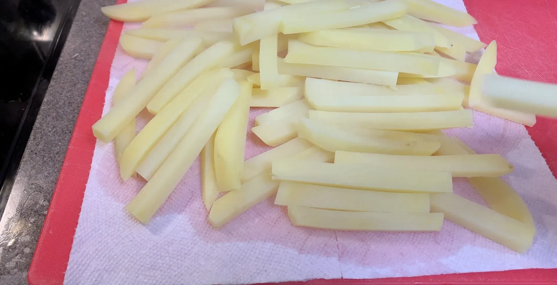 Raw potato fries cut into sticks and arranged on pink paper towels for drying before air frying.