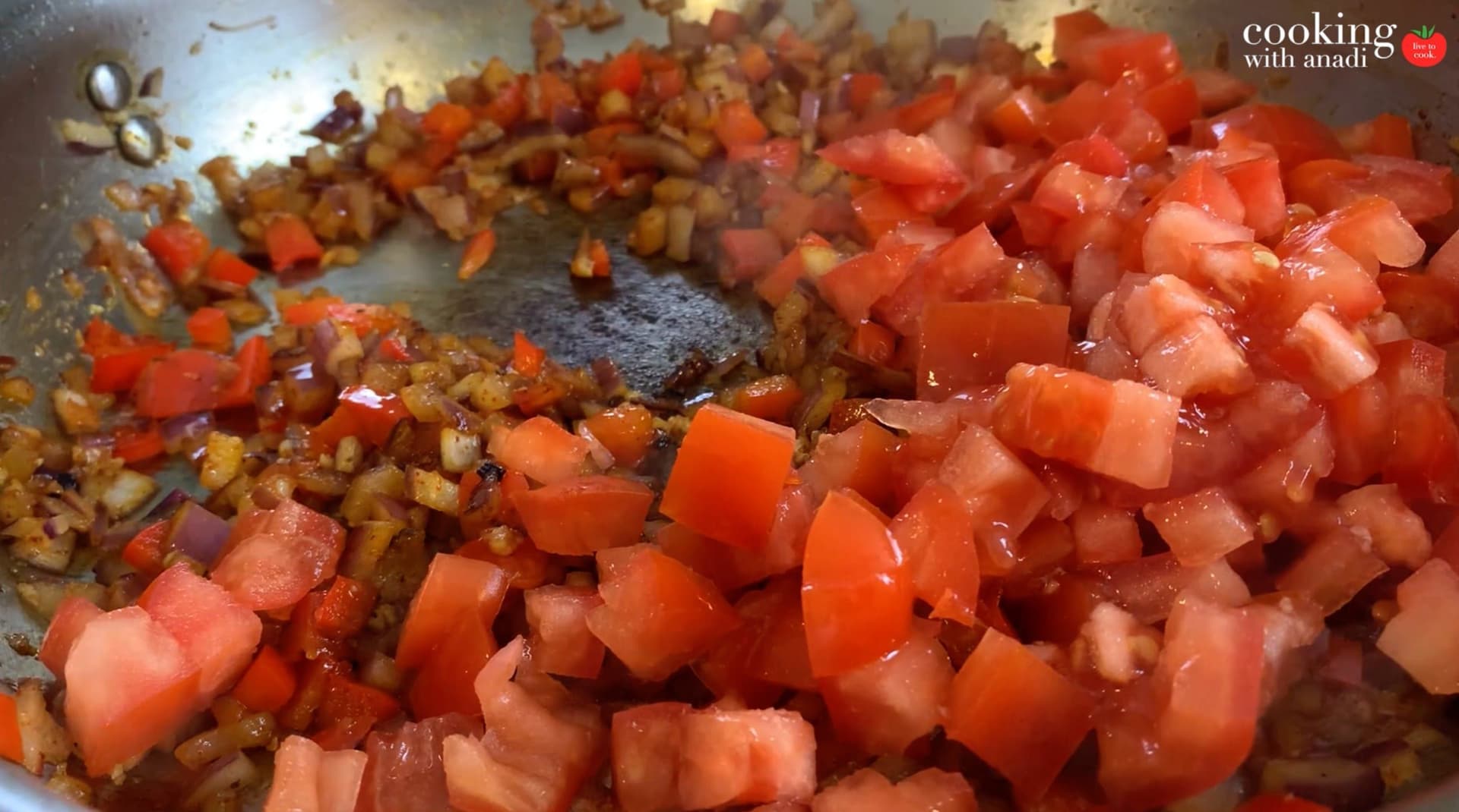 Diced tomatoes and sautéed onions, garlic, and peppers cooking together in a pan.