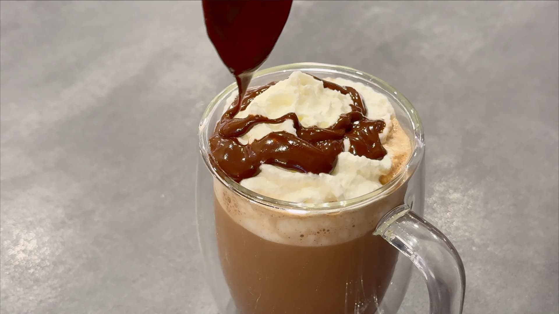 Mocha chocolate syrup being drizzled over whipped cream in a glass mug of coffee drink.