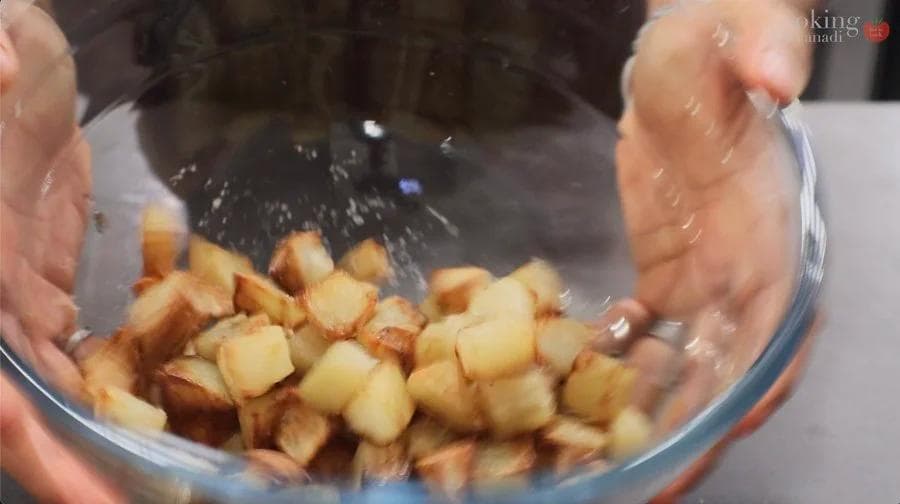 Golden-brown roasted potato cubes being tossed in a bowl during the seasoning step.