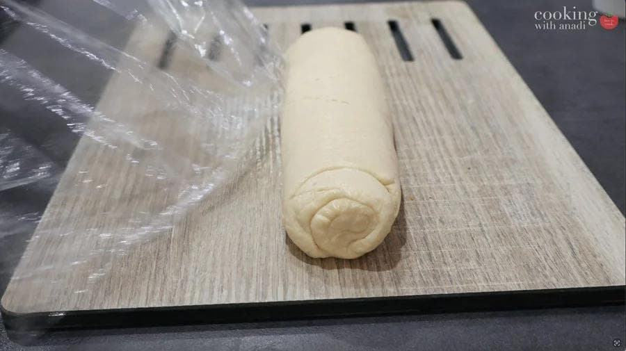 Rolled mashed potato and crescent dough log on a wooden cutting board, ready to be sliced into pinwheels.
